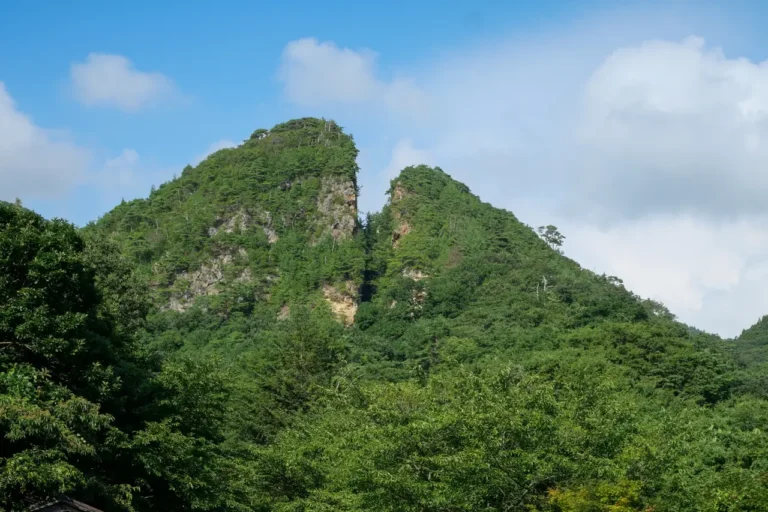 The split rocky peak of Doyu-no-Warito at Sado Kinzan, surrounded by green forest.