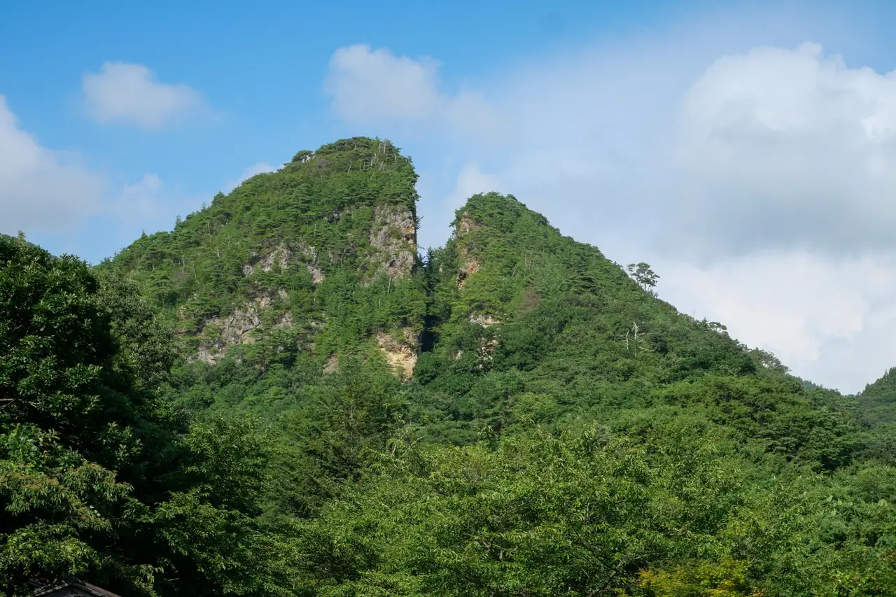 The split rocky peak of Doyu-no-Warito at Sado Kinzan, surrounded by green forest.