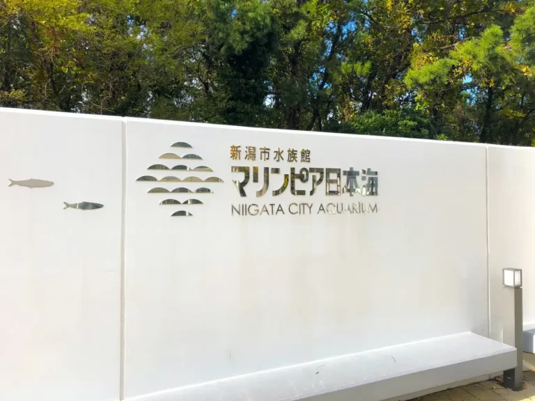White entrance sign for Marinepia Nihonkai, Niigata City Aquarium, beside green trees