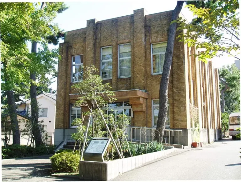 The brick exterior of Niigata University Asahimachi Museum framed by pine trees and greenery.