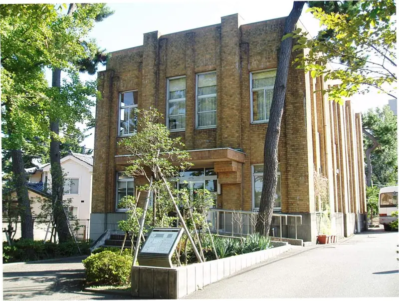 The brick exterior of Niigata University Asahimachi Museum framed by pine trees and greenery.