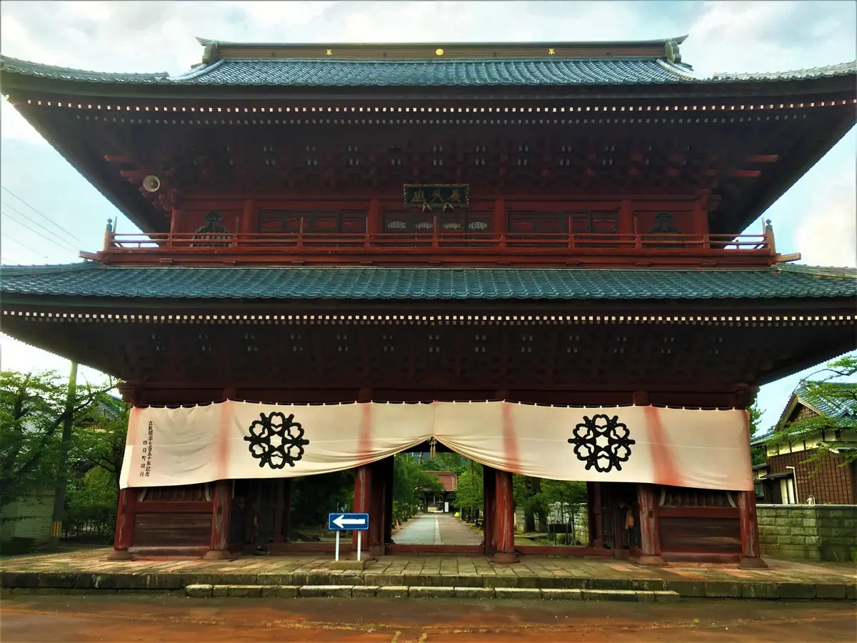 Red two-storey main gate framing the approach to Honjoji Temple in Sanjo