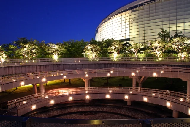 Illuminated walkways and trees beside Ryutopia at blue hour