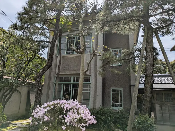 The Western-style house behind pine trees and flowering shrubs at the Northern Culture Museum Niigata Branch.