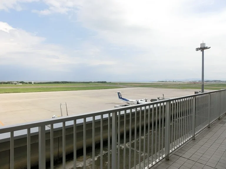 The railing of Niigata Airport’s observation deck overlooking the apron, an aircraft and the flat airfield.