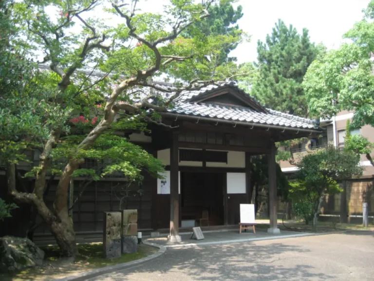 The tiled-roof entrance of Sakyukan, framed by mature trees and garden greenery.
