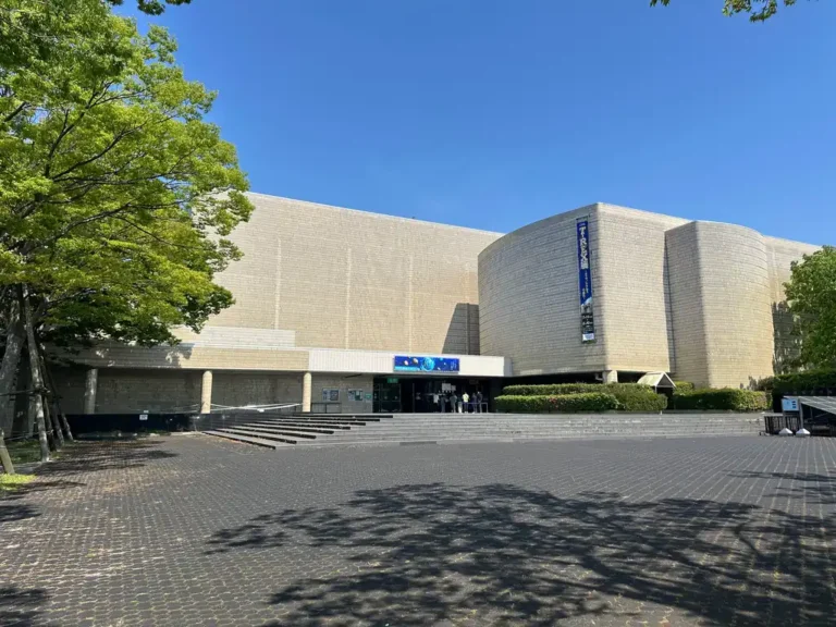 The entrance and exterior of Niigata Science Museum, with leafy trees and a paved forecourt under a clear blue sky.