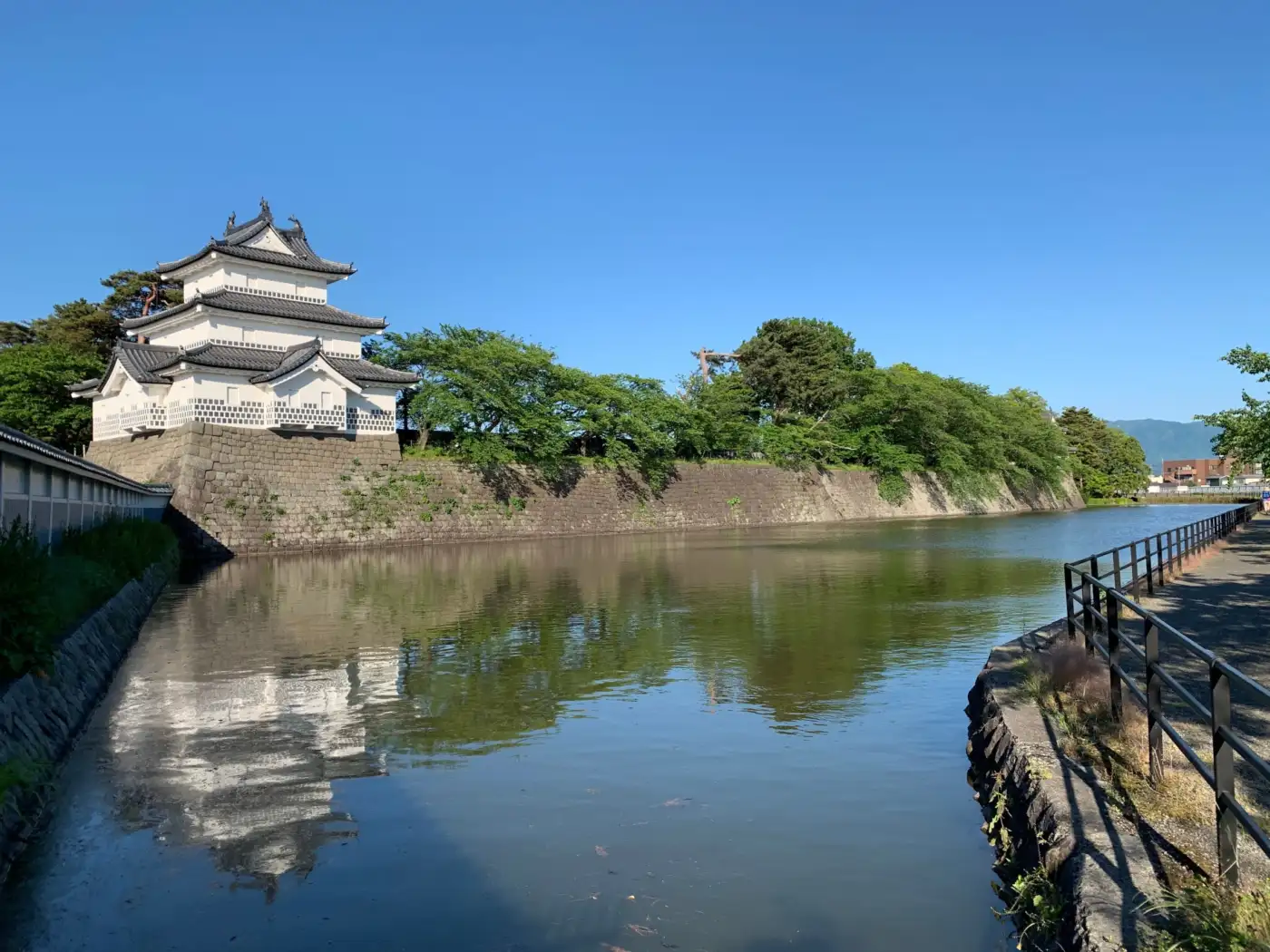 Shibata Castle’s reconstructed three-storey turret rises above a stone wall beside the moat, with its reflection visible in the water.