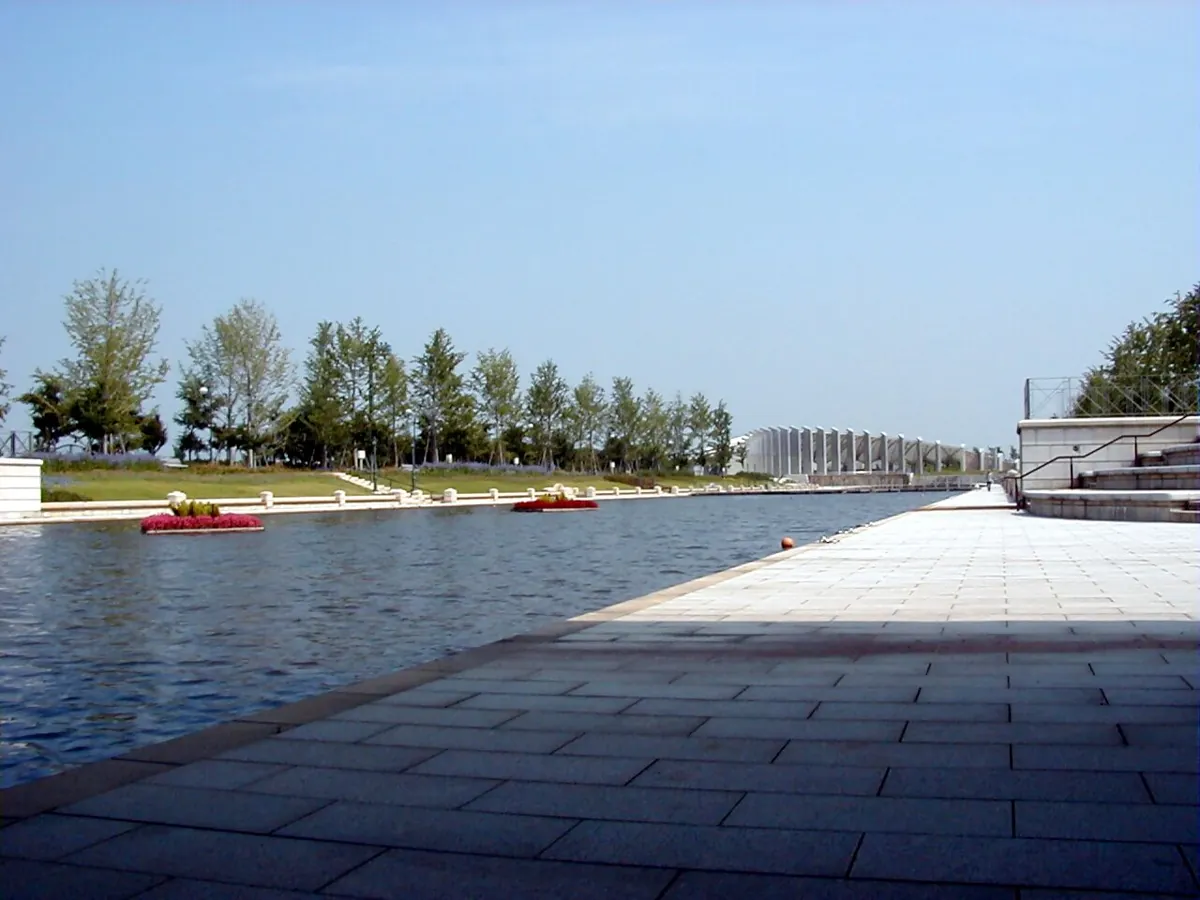 The canal and broad waterside promenade at Niigata Prefectural Sports Park, with the stadium beyond.
