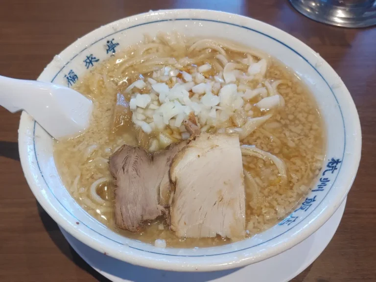A bowl of ramen topped with chopped onion and slices of pork in a rich-looking broth.