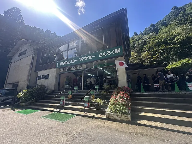The base station of Yahiko Ropeway stands beneath wooded slopes, with steps leading to the entrance.