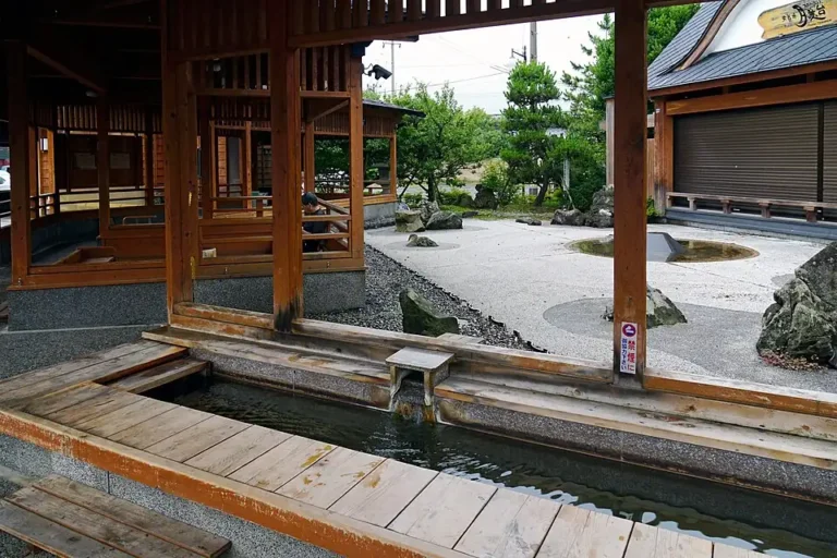 Wooden seating surrounds the Yutabi hot-spring footbath in Tsukioka Onsen, with a garden beyond.